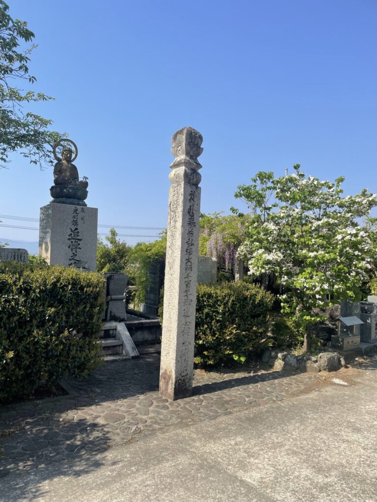境内の石柱と追悼之碑。青空のもと、ハナミズキと藤が咲いていた。